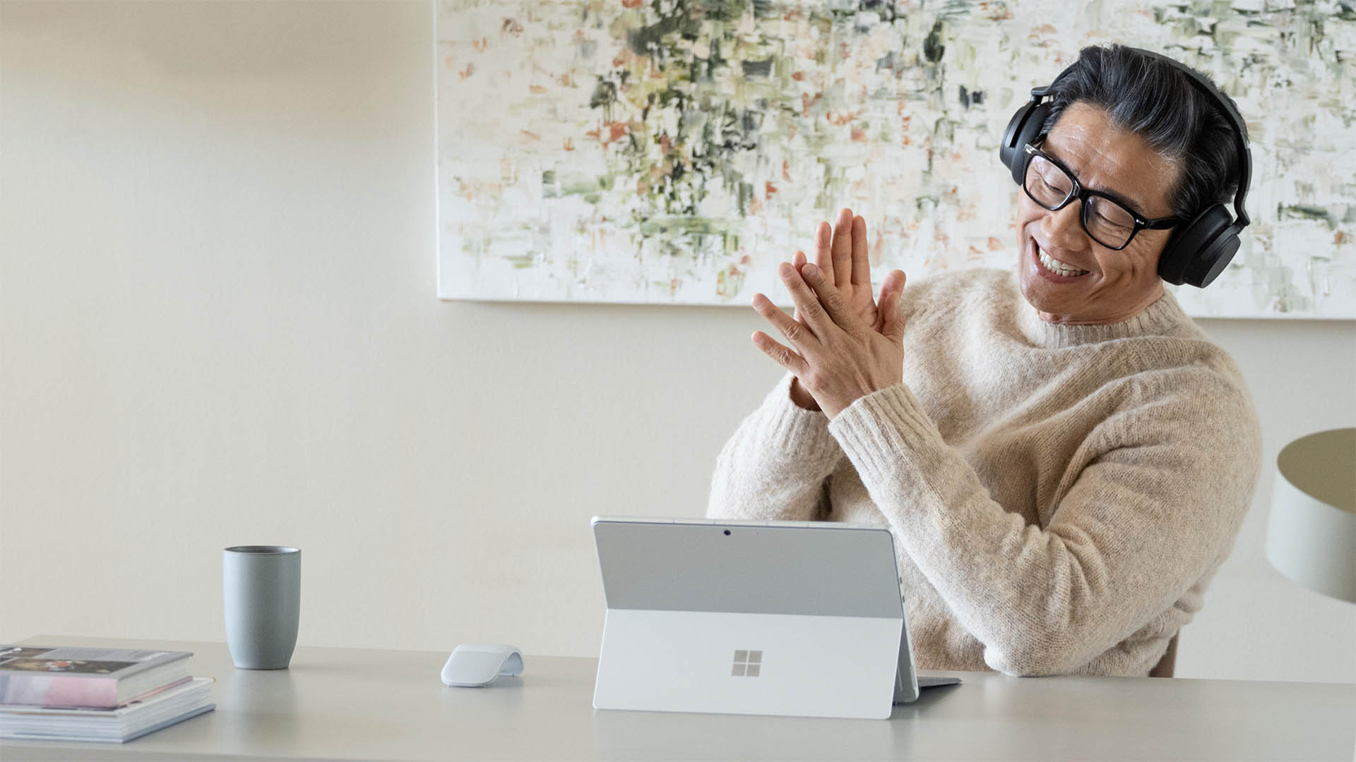 Een man, lachend en met een koptelefoon op, zit aan een tafel voor een Surface-tablet