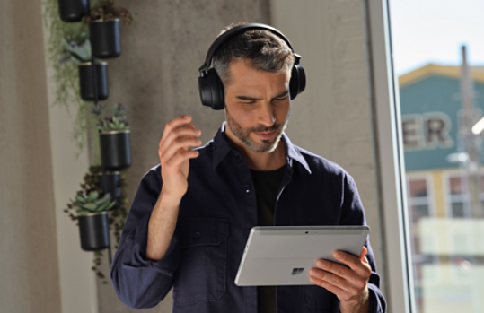 A man standing and listening to headphones while holding his Surface device