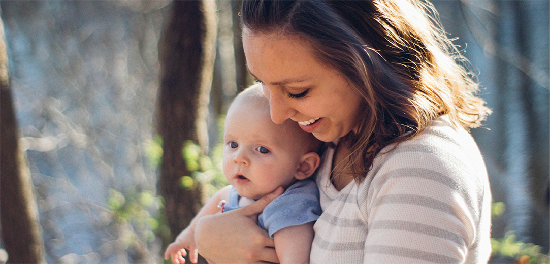 A mom carrying baby outdoors near trees