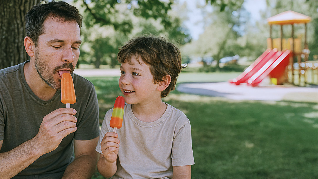 A parent and child enjoying popsicles in the shade on a summer day after using Copilot features to plan their outing