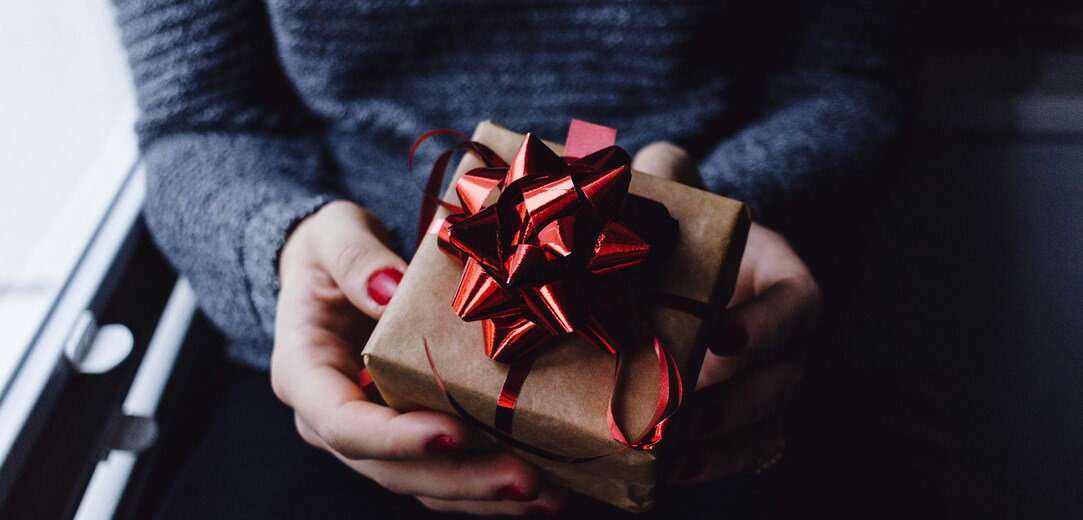 A person holds a box wrapped in brown butcher paper with a shiny red bow on top