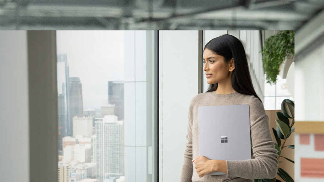 Eine Person hält ihr Surface Laptop 5 mit einem Arm an den Körper und schaut sich im Raum um