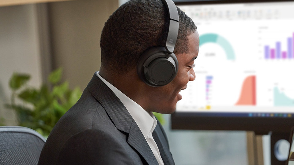 A person is seen wearing Surface Headphones 2+ while interacting on a Microsoft Teams call