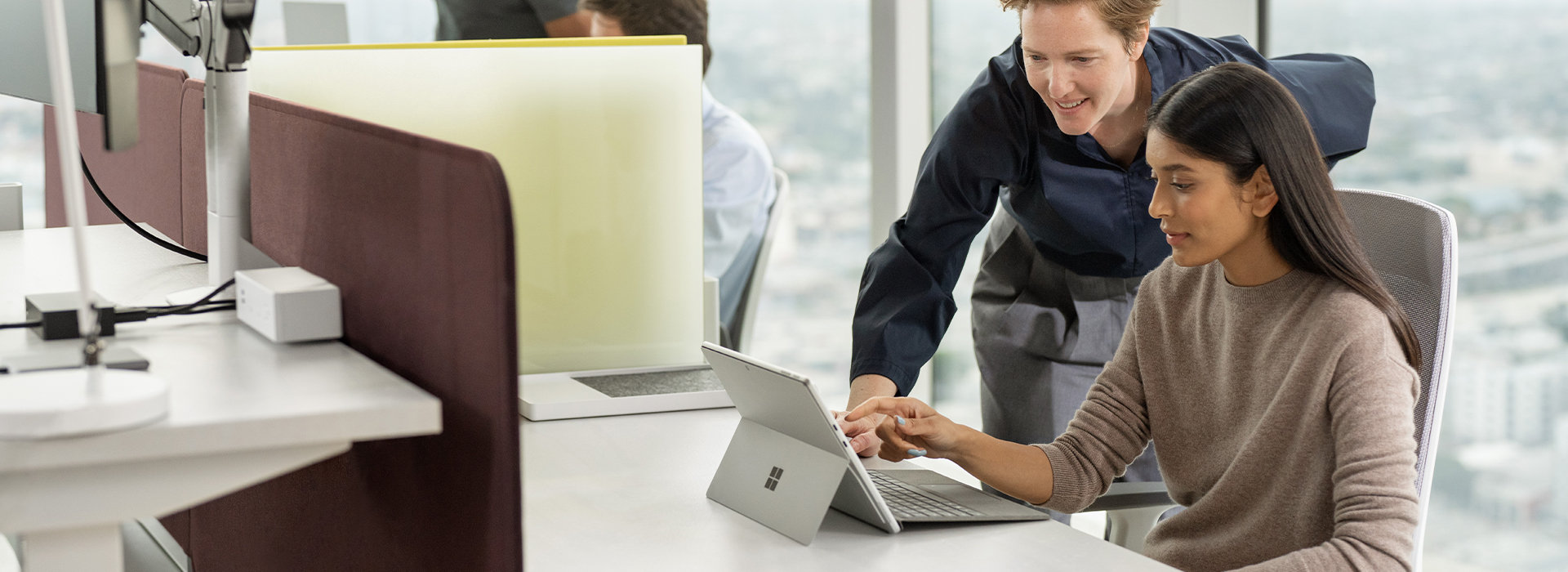 Een persoon kijkt mee over de schouder van iemand die aan een bureau zit en op het scherm van een Surface-apparaat bezig is