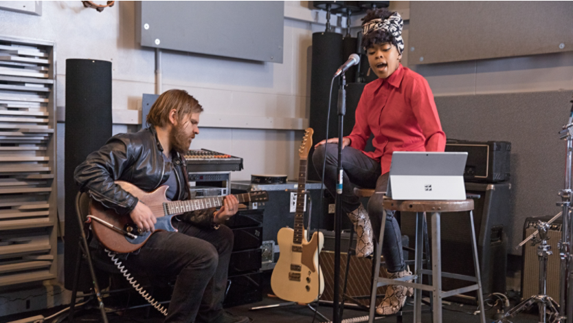 A person playing guitar and a person singing into a microphone while using a Surface 2-in-1 device