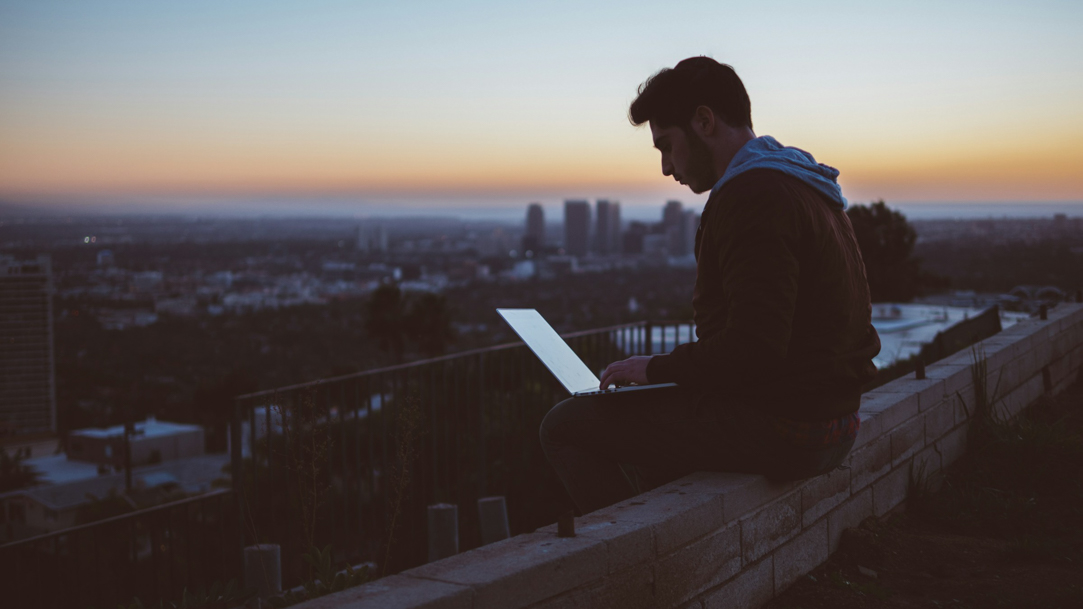 A person sitting on a ledge using a computer