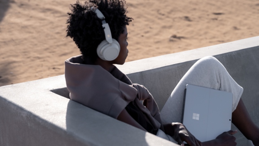 A person wearing headphones and using a Surface device outdoors