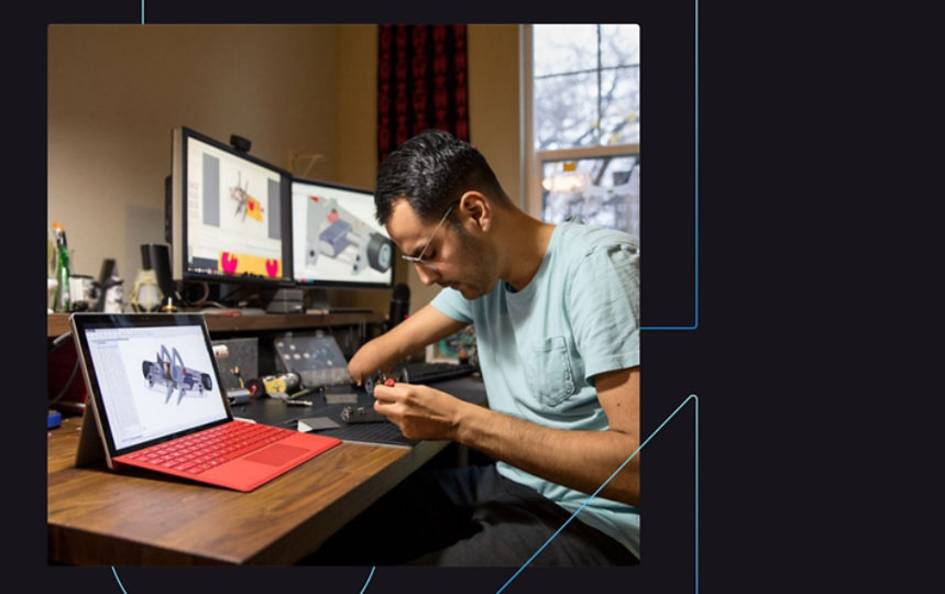 男士坐在办公桌前，用双显示器和笔记材料工作。