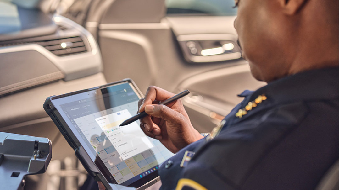 A policeman is shown in his patrol car using Surface Pen to write on his Surface Pro device
