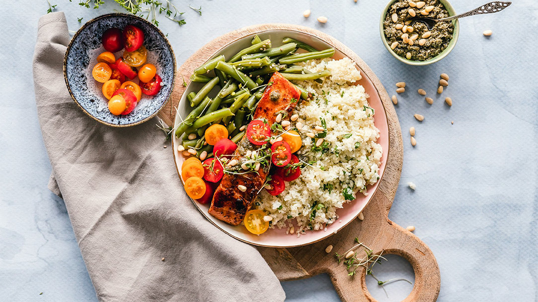 A top-down photo of a bowl with rice, green beans, tomatoes, and grilled salmon on a countertop