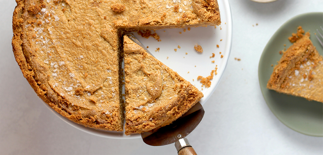 A top-down view of a baked pie on a white stand, with a white plate on the side
