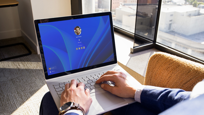 Un utilisateur tenant un ordinateur portable ouvert et accueilli par l’écran de connexion Windows Hello.