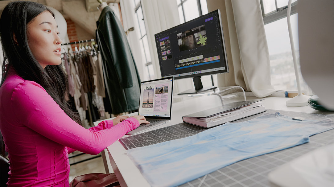 A woman at a desk with two computers, using Microsoft Edge battery saver performance settings