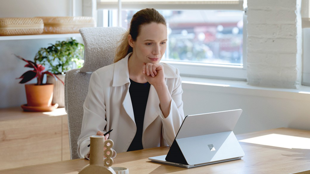 امرأة تحمل جهاز Surface Pro وتتحدث مع امرأة أخرى في مكتب موظف الاستقبال