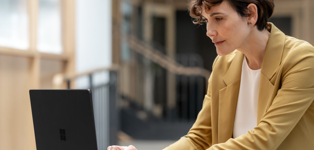 A woman in a yellow suit scrolls on a black Surface laptop