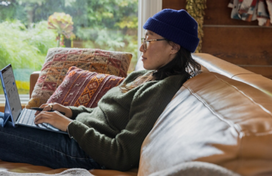 A woman sitting on a couch works on her Surface device