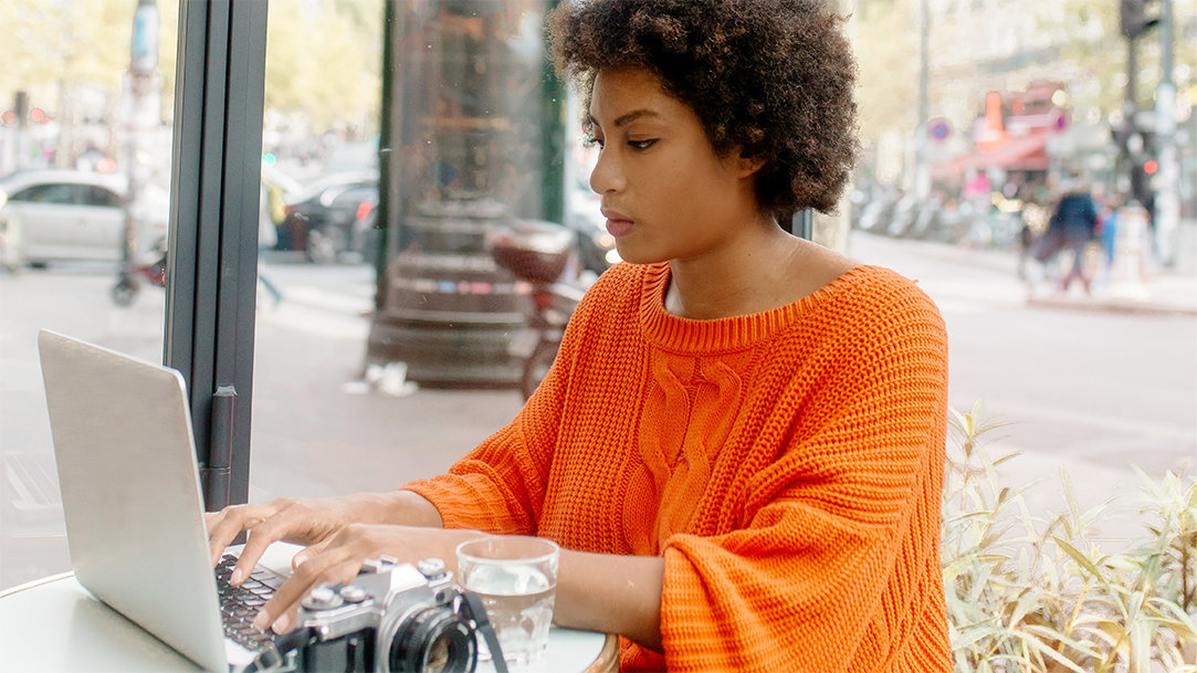 A woman sitting outdoors at a cafe, typing on a laptop