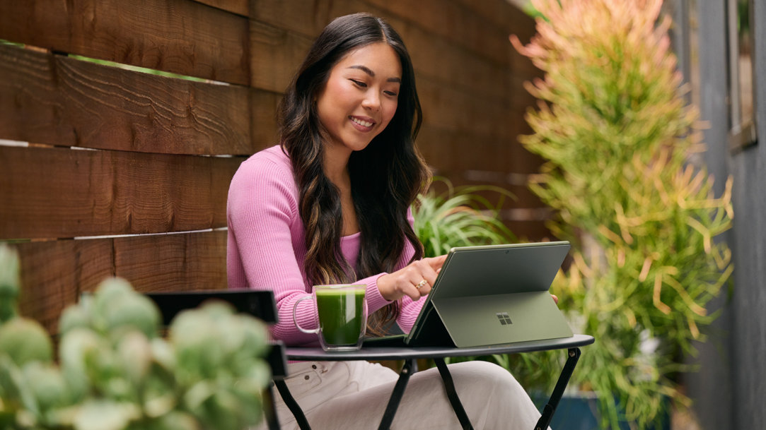 A woman sitting outside while using a Microsoft Surface Pro 9