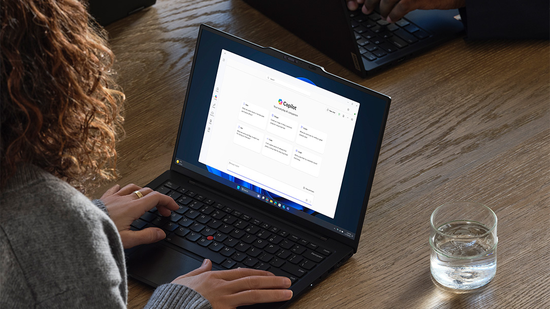 A woman typing into Copilot on her Lenovo laptop while working in an office space