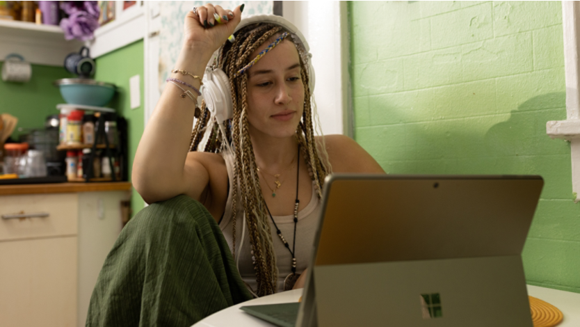 A woman with braids sitting in front of a laptop computer with headphones on