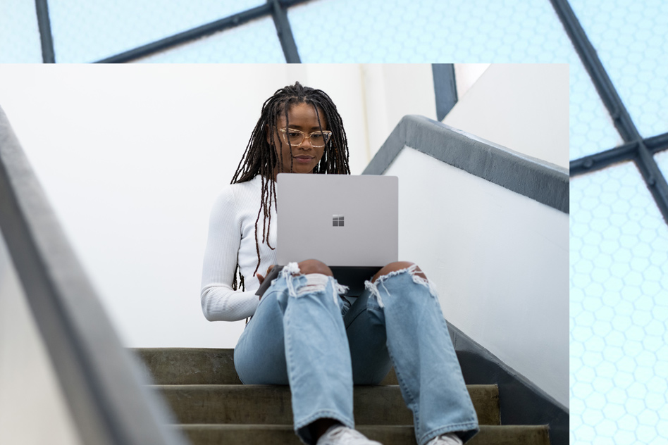 A woman works on her Platinum Surface Laptop 5 in a staircase.