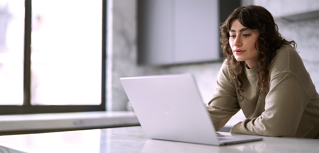 A woman works on her laptop in a kitchen setting