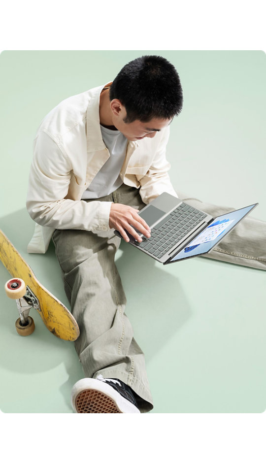 スケートボードを中断し、Surface Laptop Go 2 で素早くメッセージをタイプする若い男性。