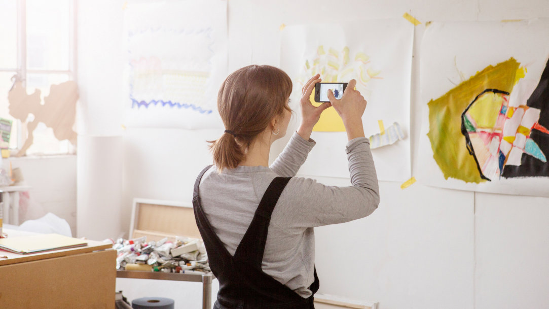 An artist takes a photo on her phone of painting and sketches