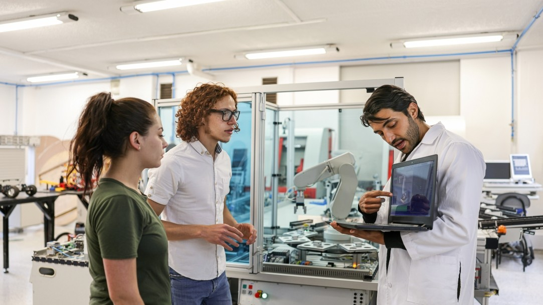 An educator using a laptop with two of his students in a lab