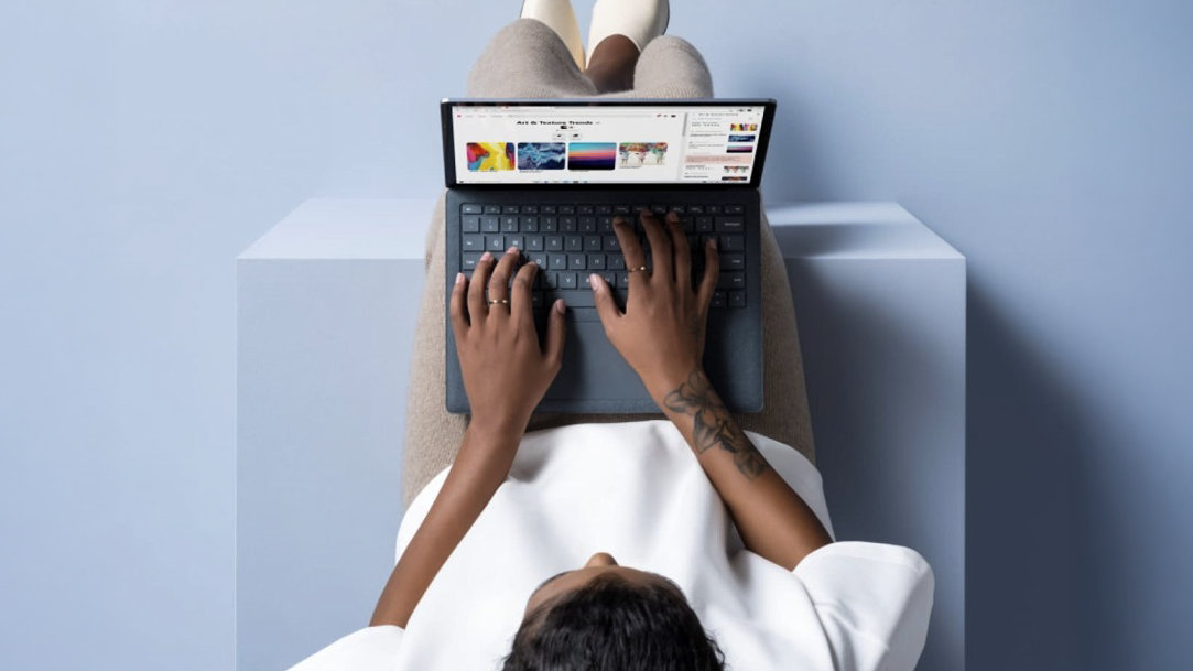 An image from the top looking down to a woman lying on her back with a laptop and browsing the web