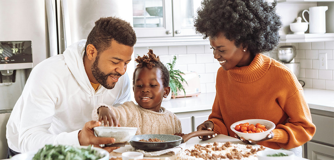 An image of a family together in the kitchen preparing pizza