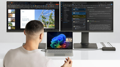 An image of a man using a Surface Laptop Copilot+ PC and dual monitors connected via a Surface dock