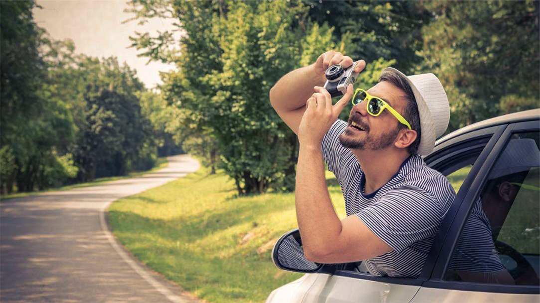 An image of a man with a camera leaning out of a car to take a picture