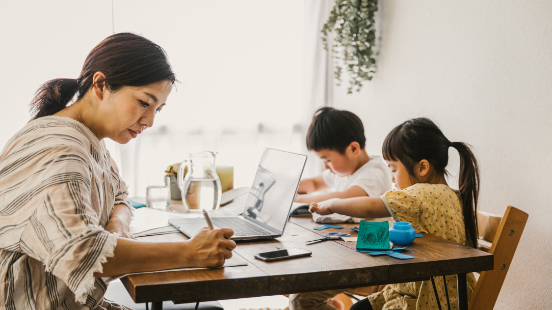 An image of a stay-at-home mom with the ability to multitask by taking care of home business on a laptop and overseeing her children’s school activities