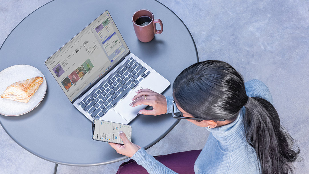 An image of a woman drinking coffee and eating a snack, while browsing the web on a laptop and using a smart phone