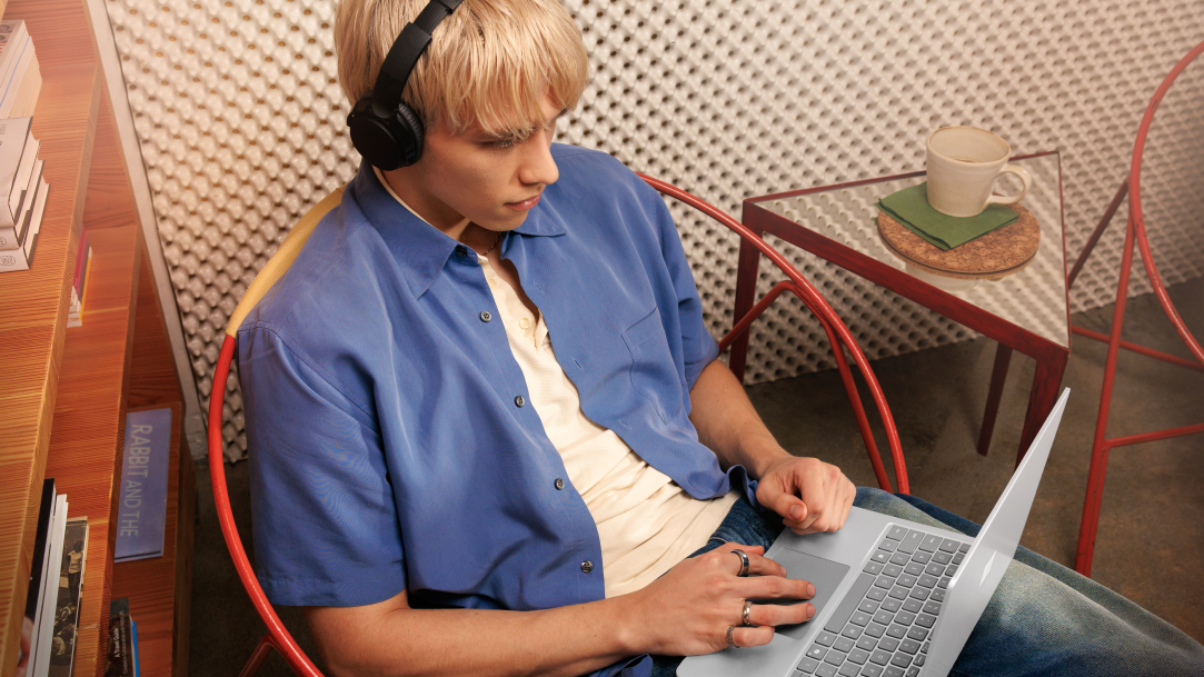 An image of a young adult man wearing headphones and using a Surface Laptop