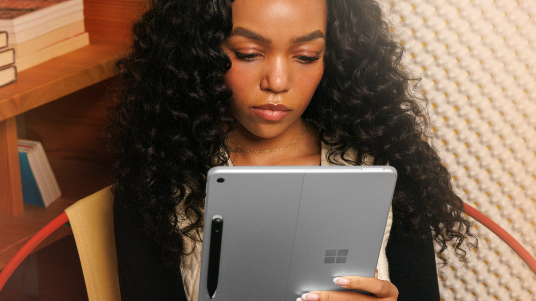 An image of two female colleagues who are doing a high-five with a glowing, yellow circle background and walking with Surface laptops in their hands