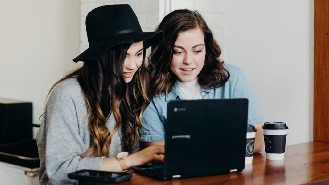 An image of two women sitting at a table innocently enjoying using their device