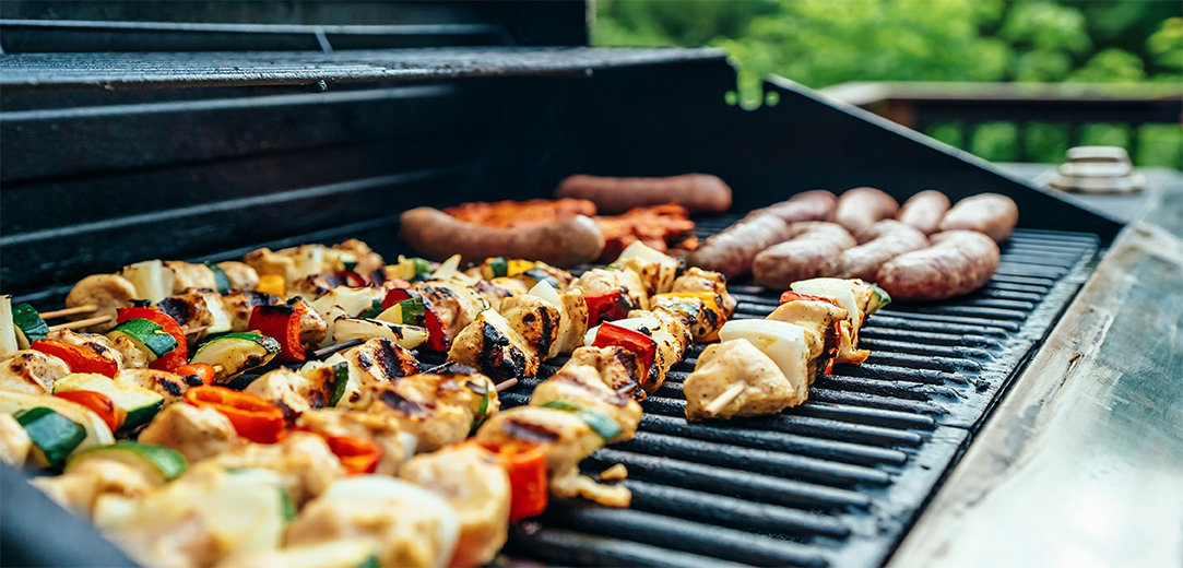 An open grill with charred vegetable skewers, bratwursts, and chicken