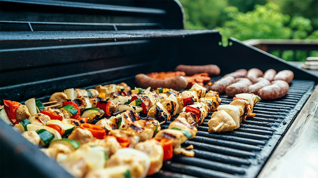 An open grill with charred vegetable skewers, bratwursts, and chicken