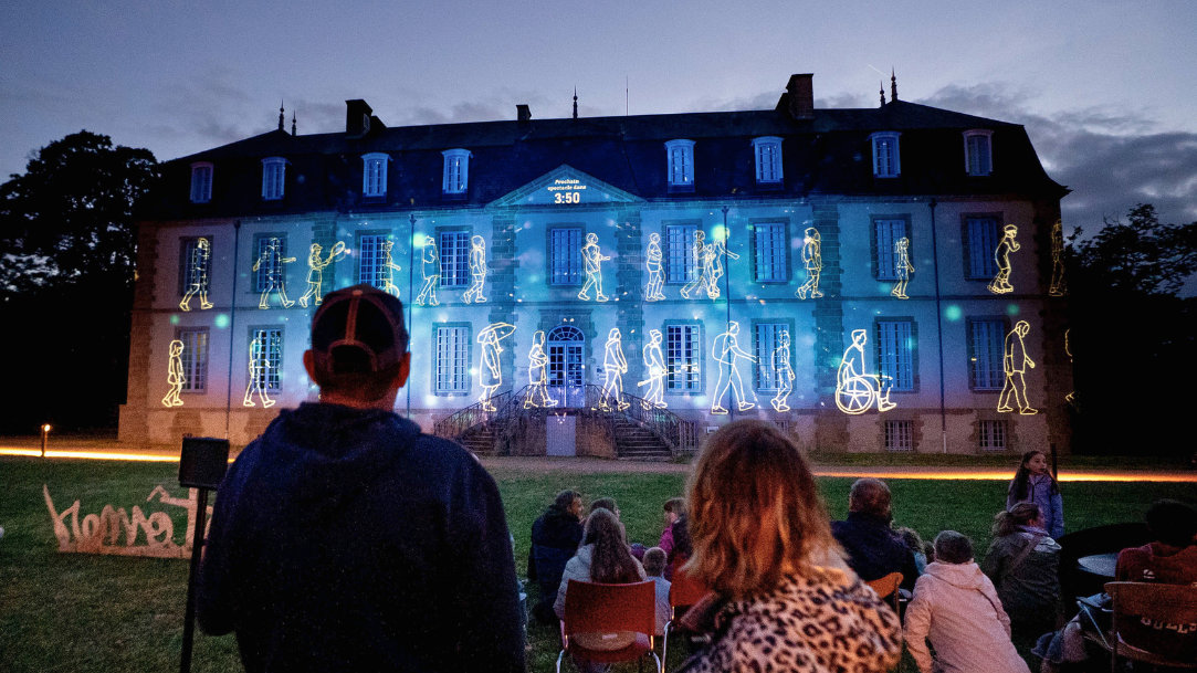 Art installation participants look on as a light show projects onto a French classical facade under the night sky