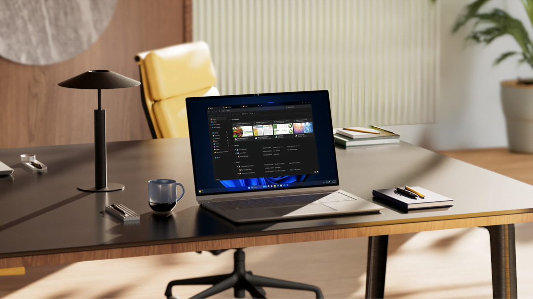 An open laptop displaying File Explorer in Windows, with tabs and AI powered recommendations in dark mode, sits on an office desk alongside notebooks and a coffee mug