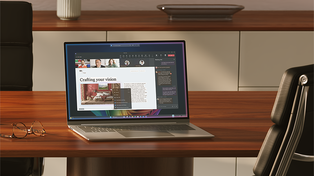 An open Windows 11 Pro PC sitting on a wood desk, with a pair of reading glasses and office chair, in a meeting room