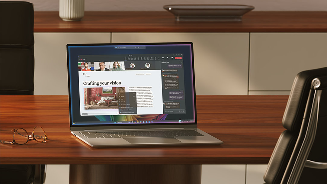 An open Windows 11 Pro PC sitting on a wood desk, with a pair of reading glasses and office chair, in a meeting room