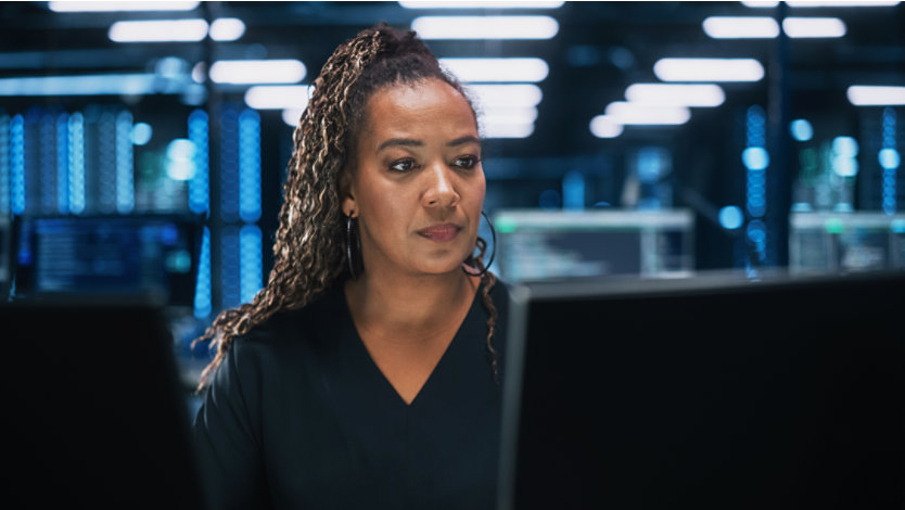 An office worker sitting in a large open office area looking at a large computer screen