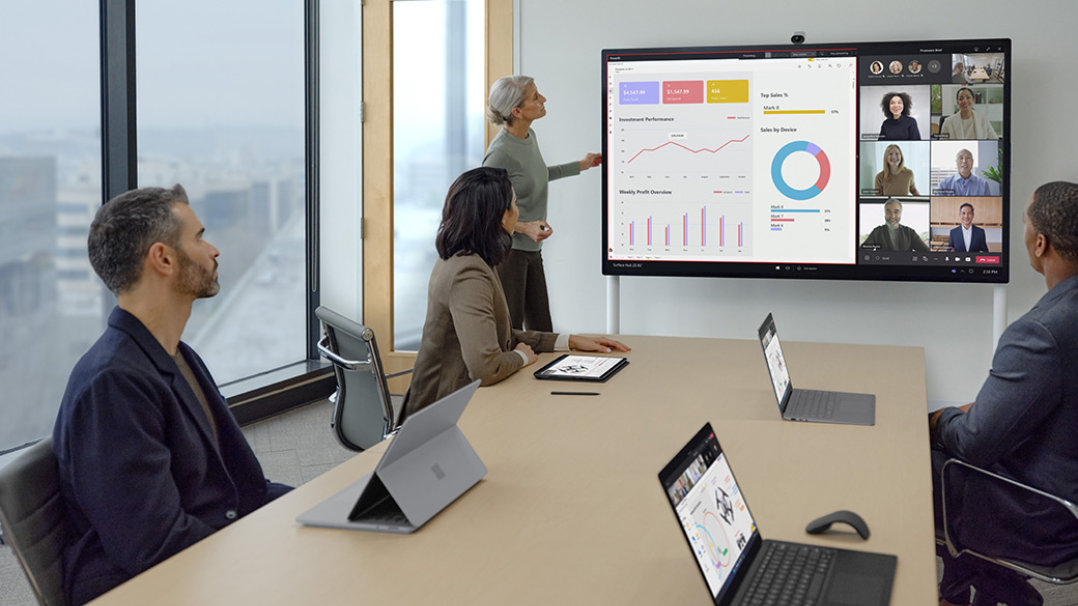 Co-workers sit at a conference table while one person uses Surface Hub 2 Pen to ink on the screen. Remote team members observe.