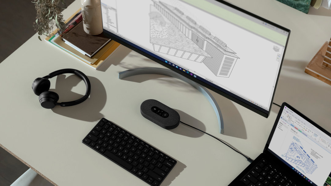 Desk with a monitor showcasing a blueprint, an open laptop, and PC accessories