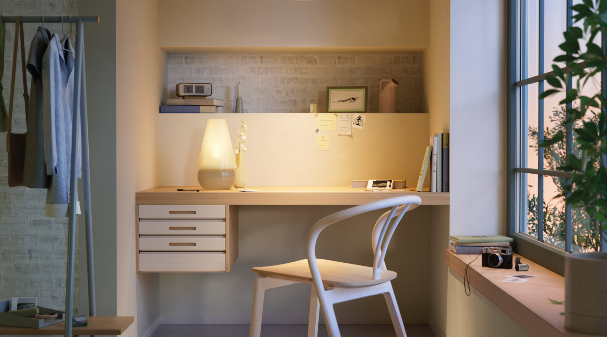 A warmly lit home office nook with a wall-mounted wooden desk, a white chair, a table lamp and a window with plants