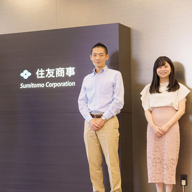 Employees of the Sumitomo Corporation are seen standing in front of the company sign in an office