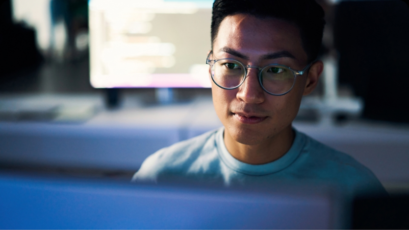 Man sitting at a desktop wearing glasses and looking at his screen.